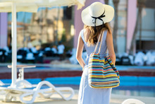 Young Woman Wearing Light Summer Dress And Yellow Straw Hat Holding Fashionable Shoulder Bag Standing Outside Hotel On Summer Sunny Day.