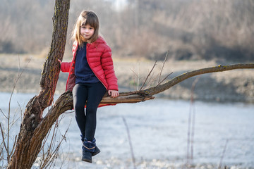 Wall Mural - Portrait of a pretty child girl sitting on a tree branch in autumn outdoors.