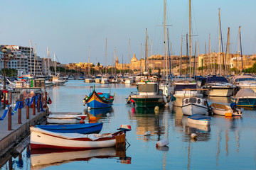 Fototapete - Valletta harbour with yachts and multicolored fishing boats Luzzu with eyes, church and fortress, illuminated by sunset light, Malta