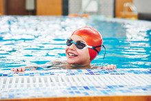 Joyful Smiling Boy Swimmer In A Cap And Goggles Learns Professional Swimming In The Swimming Pool In Gym Close Up