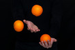 male hands juggle with fresh oranges on a dark background