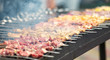 skewers with cooked and raw meat lie on the grill during the preparation of barbecue in large quantities