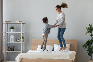 Canvas Print - Happy mixed race mother and little son jumping on bed