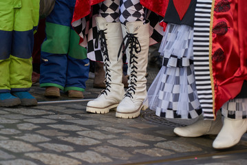 feet of different persons at carnival parade - especially a pair of legs with long white boots with black laces