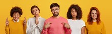 Unimpressed Bearded Man Points At Himself, Four Women Stand Near Him, Pray And Beg For Something, Have Glad Expressions, Wear Spectacles, Isolated Over Yellow Background. Body Language, Emotions