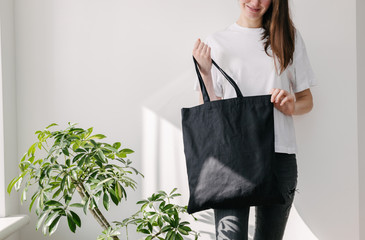 young woman holding black textile eco bag againstwhite wall. ecology or environment protection conce
