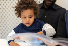 Cute Little Mixed-race Child Flipping Through A Fairy Tale Book In His Father's Arms, Details About The Child's Curious Expression, Concept Of Parental Home Education