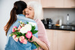 © Yakobchuk Olena - Cheerful old lady holding flowers and hugging granddaughter