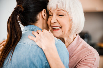 Wall Mural - Cheerful elderly woman hugging granddaughter and smiling