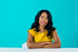 © Carlos David - Portrait of a young woman sitting behind table looking up thinking isolated on blue copy space