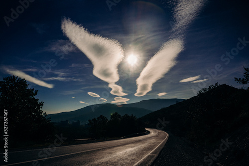 Clouds resembling angel wings and the sun in the blue sky between them. Mountain road leading to Sukko villages