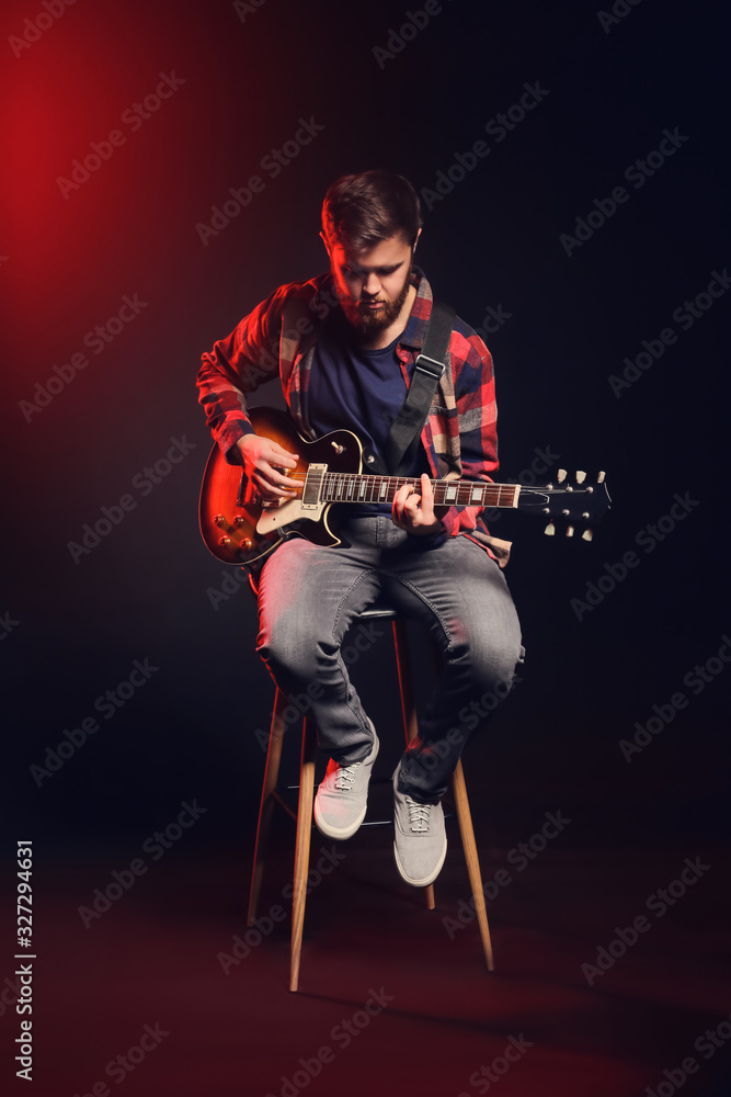 Young man playing guitar on dark background