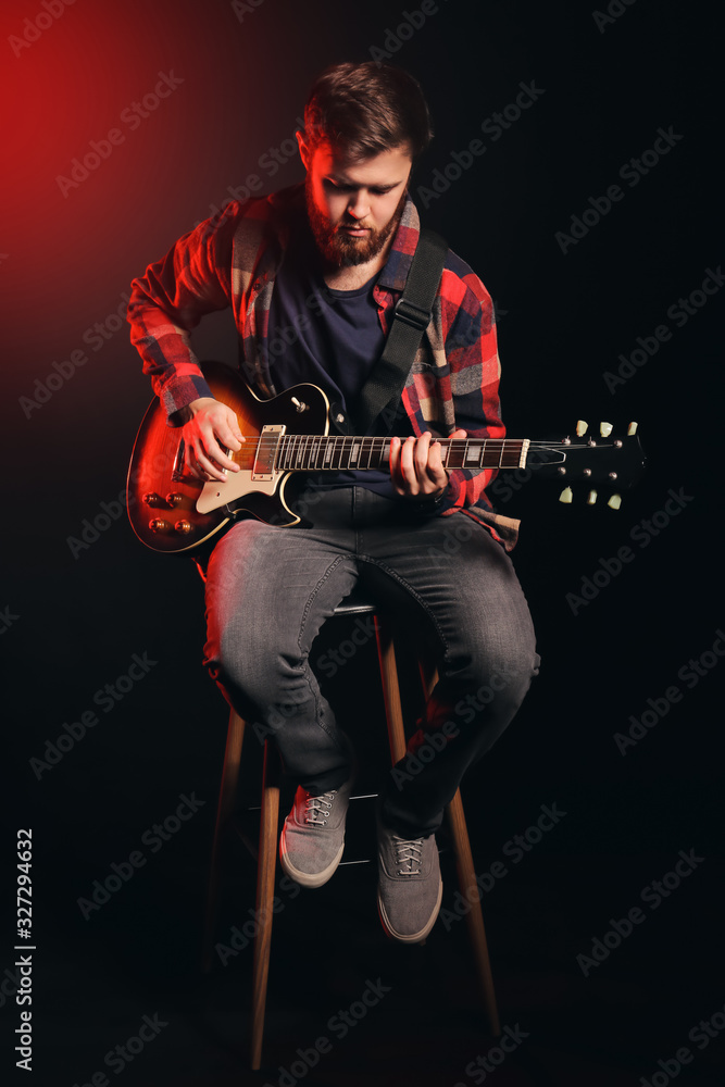Young man playing guitar on dark background