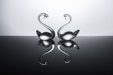 two transparent glass swans on a glossy surface