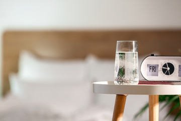 Glass of water and alarm clock on table in bedroom