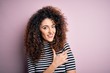 © Krakenimages.com - Young beautiful woman with curly hair and piercing wearing casual striped t-shirt cheerful with a smile of face pointing with hand and finger up to the side with happy and natural expression on face