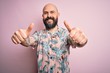 © Krakenimages.com - Handsome bald man with beard and tattoo wearing casual floral shirt over pink background approving doing positive gesture with hand, thumbs up smiling and happy for success. Winner gesture.