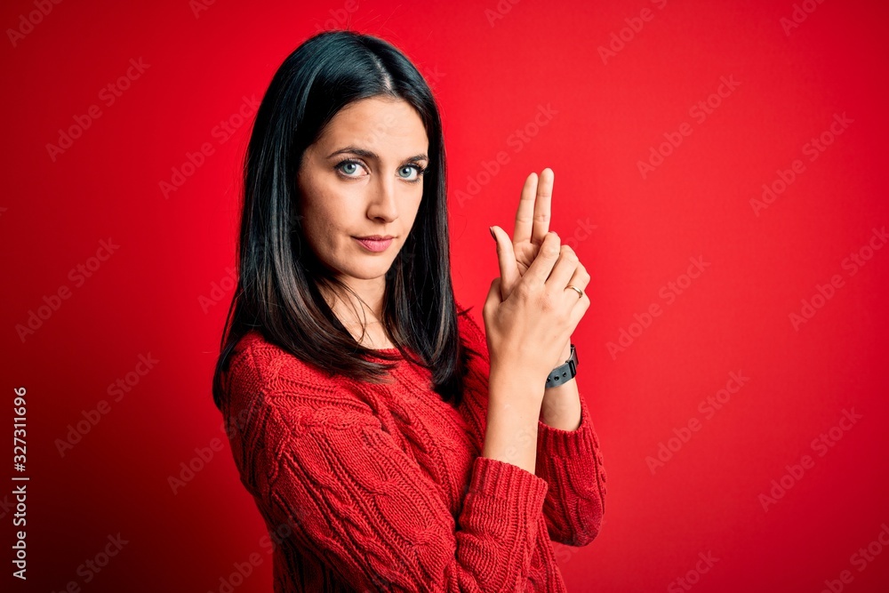 Young brunette woman with blue eyes wearing casual sweater over isolated red background Holding symbolic gun with hand gesture, playing killing shooting weapons, angry face