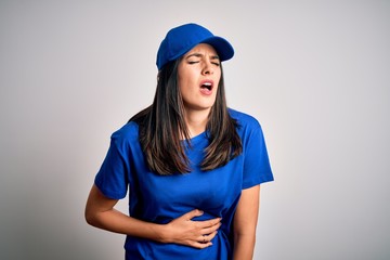 Young delivery woman with blue eyes wearing cap standing over blue background with hand on stomach because nausea, painful disease feeling unwell. Ache concept.