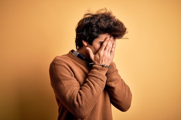 Young handsome man wearing casual shirt and sweater over isolated yellow background with sad expression covering face with hands while crying. Depression concept.