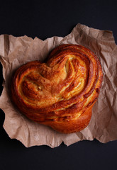 Fresh sweet bun in the shape of a heart on a dark background