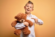 Young Little Caucasian Kid Hugging Teddy Bear Stuffed Animal Over Yellow Background Very Happy Pointing With Hand And Finger
