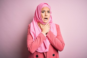 Poster - Young beautiful girl wearing muslim hijab standing over isolated pink background shouting suffocate because painful strangle. Health problem. Asphyxiate and suicide concept.