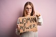 © Krakenimages.com - Young beautiful redhead woman asking for women rights holding banner over pink background pointing with finger to the camera and to you, hand sign, positive and confident gesture from the front