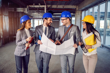 Wall Mural - Small group of dedicated highly motivated architects walking in building they want to renew and talking about new ideas to correct blueprints.