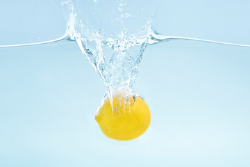 Fresh citrus fruit. Ripe lemon falling into water on blue background