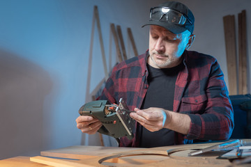 Joinery. A person changes the nozzle in an electric jigsaw. Woodworking. Manufacture of products from wood and plywood. Carpentry tools. A man is preparing to cut plywood.