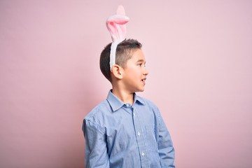 Sticker - Young little boy kid wearing easter bunny ears over isolated pink background looking away to side with smile on face, natural expression. Laughing confident.