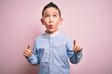 Sticker - Young little boy kid wearing elegant shirt standing over pink isolated background amazed and surprised looking up and pointing with fingers and raised arms.