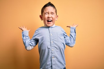 Sticker - Young little boy kid wearing elegant shirt standing over yellow isolated background celebrating mad and crazy for success with arms raised and closed eyes screaming excited. Winner concept