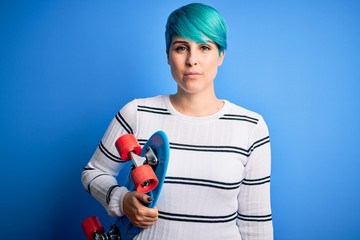 Sticker - Young skater woman with blue fashion hair holding skateboard over blue isolated background with a confident expression on smart face thinking serious