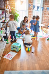 Wall Mural - Beautiful teacher and group of toddlers playing around lots of toys at kindergarten