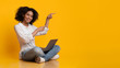 © Prostock-studio - Cheerful Afro Girl Sitting On Floor With Laptop And Pointing Aside