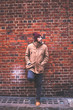 © javiemebravo - Young man with hat and warm clothes leaning against brick wall looking sideways in a London street