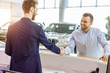 © Roman - young caucasian customer man shake hand to pleasant nice consultant. handsome consultant welcomes buyer, going to help him with choice of car