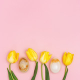 Fototapeta Tulipany - Decorative Easter eggs and spring yellow fresh flowers tulip on pink background with copy space. Happy Easter card. Flat lay, top view.
