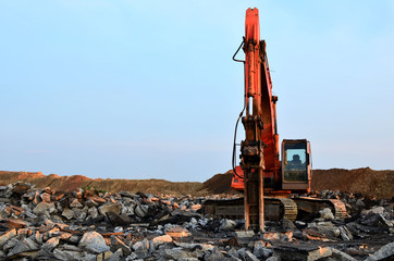 Heavy excavator working at gravel quarry unloads old concrete stones for crushing and recycling to gravel or cement. Special heavy construction equipment for road construction.