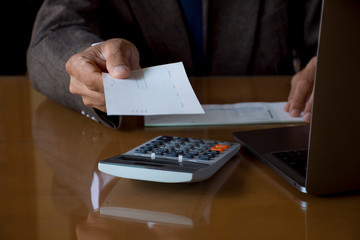 Wall Mural - Businessman or manager in suit hand holding and giving blank bank check book to the other person with calculation machine and laptop computer on the desk at office. Paycheck and payroll concept.