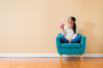 Wall Mural - Young woman with a piggy bank sitting in a chair