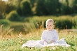 © Sunshine - A small child sits on a blanket on the shore of the lake in the open air. Summer walks with the baby. Copying space