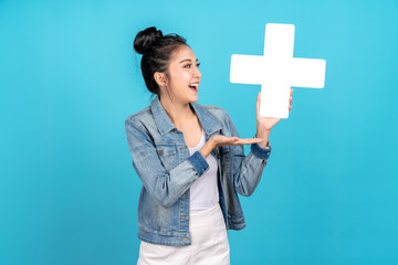 Wall Mural - Happiness asian woman smiling, showing plus or add sign and other hand open on blue background. Cute asia girl wearing casual jeans shirt and showing join sign for increse and more benefit concept