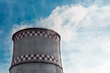 Cooling tower, desuperheater, smoke from a pipe of an industrial plant or thermal power plant on a background of blue sky with clouds