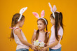 © producer - happy little child girls with pink bunny ears holding basket with painted Easter eggs on studio background. Easter day