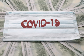 Medical mask laying on dollars, concept of increasing costs for protection of virus like the coronavirus or Covid19.