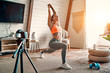 © Valerii Apetroaiei - Athletic woman blogger in sportswear shoots video on camera as she does exercises at home in the living room. Sport and recreation concept. Healthy lifestyle.