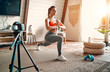 © Valerii Apetroaiei - Athletic woman blogger in sportswear shoots video on camera as she does exercises at home in the living room. Sport and recreation concept. Healthy lifestyle.
